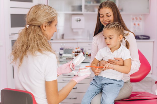 Child learning about oral hygiene during a dental visit with her mother, representing a kids dental clinic near me Katy for gentle pediatric dental care